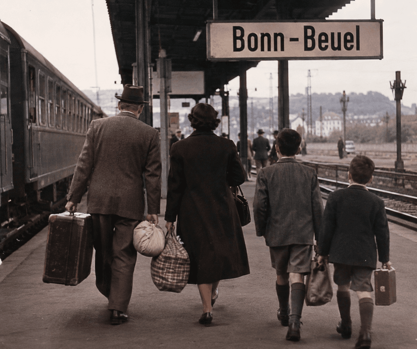 Familia caminando por un andén de tren en la estación de Bonn-Beuel, Alemania, con maletas