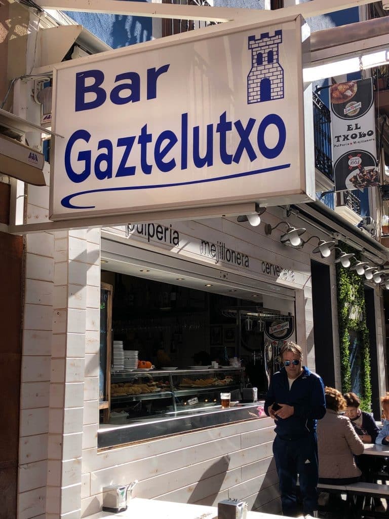 Cartel del Bar Gaztelutxo, en la calle Santo Domingo, con la barra de pintxos detrás