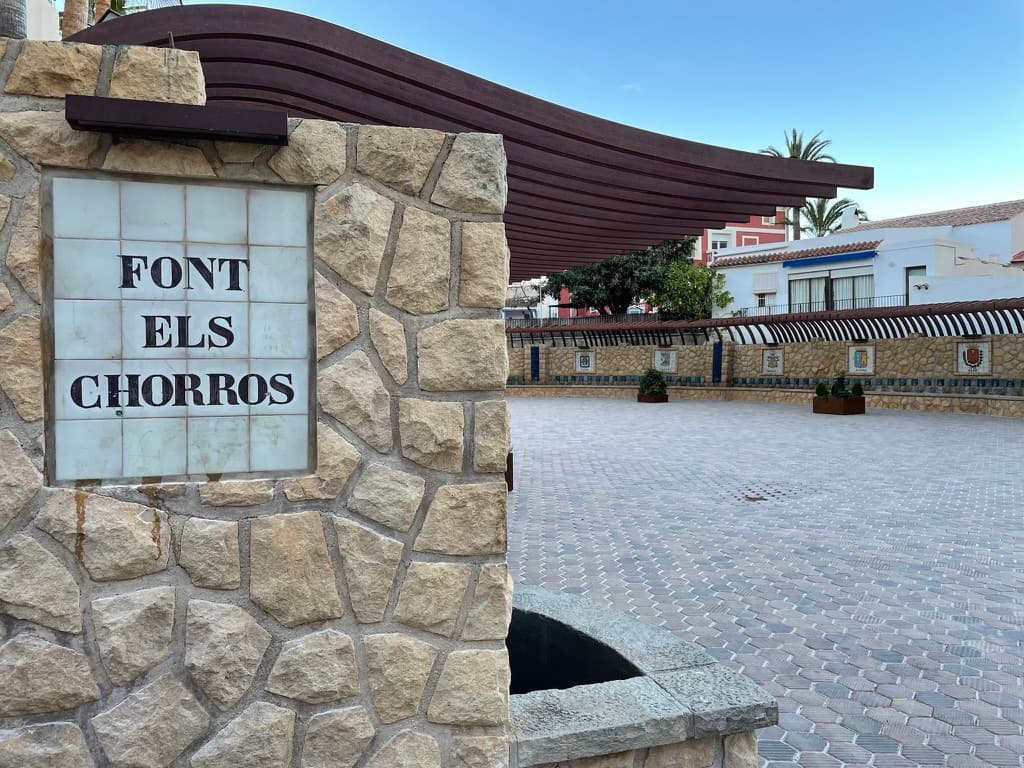 Plaza de la Font els Chorros de Polop, con el rótulo de la fuente y el muro de caños al fondo
