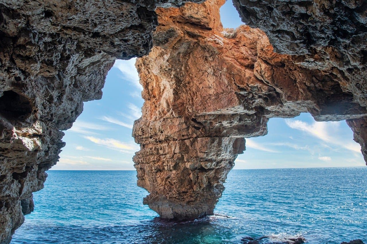 Vista dal mare dell'arco di pietra della Cova dels Arcs, ideale da esplorare in kayak o con lo snorkeling
